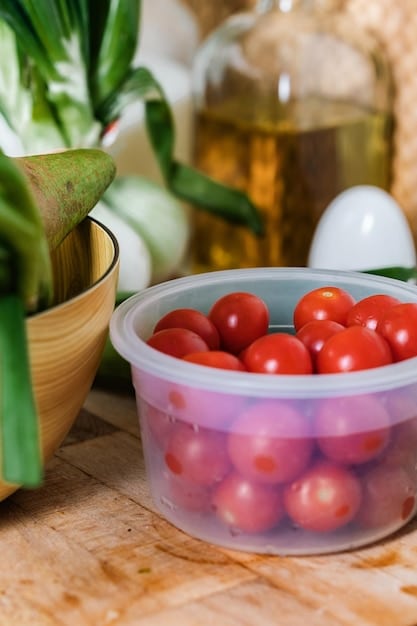 A close-up shot of a variety of reusable food storage containers (glass and stainless steel) filled with colorful fruits and vegetables. The containers are neatly arranged on a kitchen counter.