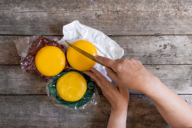A close-up shot of a person replacing plastic wrap with reusable beeswax wraps on a bowl of leftovers. The focus is on the texture and vibrant colors of the beeswax wraps.