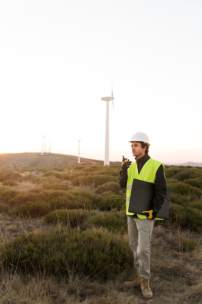An engineer inspecting a wind turbine high in the mountains, with a clear blue sky in the background, symbolizing the technology and expertise required for clean energy projects.