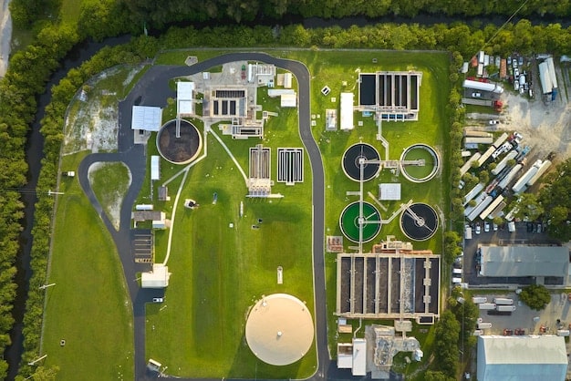 An aerial shot of a modern biogas plant, showing large digesters and associated infrastructure. The plant is surrounded by farmland, with piles of agricultural waste visible nearby. The image conveys a sense of industrial efficiency and integration with agricultural practices.