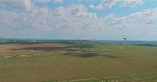 An aerial view of a sprawling wind farm in a rural area, juxtaposed with a transmission line stretching towards a distant city, illustrating the challenges and infrastructure needs associated with scaling up renewable energy production.