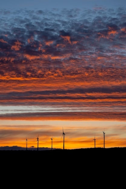 A sprawling wind farm against a dramatic sunset, with turbines actively generating electricity. The image captures the scale and efficiency of renewable energy production eligible for the Production Tax Credit.